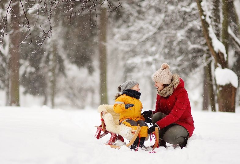 Mutter und Tochter mit Schlitten beim Spaziergang im Winter.